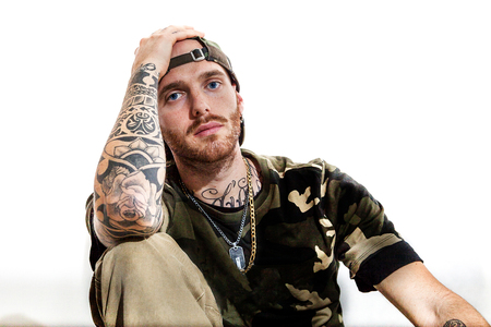 sitting tattooed rap singer posing in studio with an amplified radio on a white background