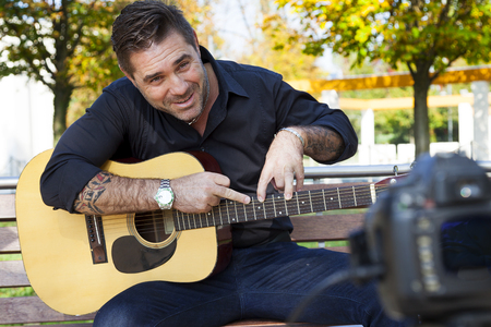 young man guitar teacher making a videos about practical guitar exercises in a public park