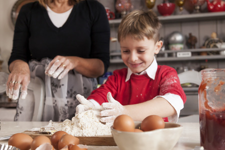Little boy having fun and prepare the dough for cookies with eggs and flour in home cooking