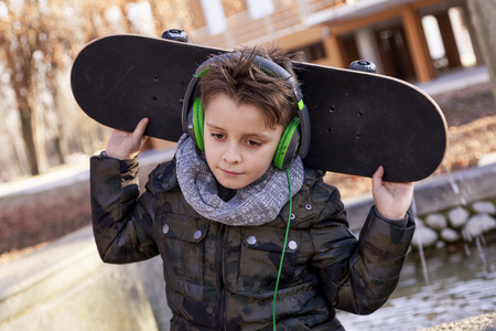 Elegant child relaxing sitting on a marble bench with his skateboard in winter outdoorsの写真素材