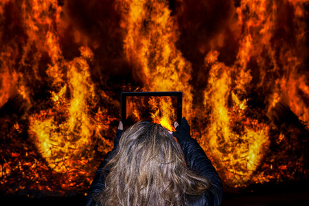 Attractive woman takes a selfie in front of a big fire during a nighttime village festival