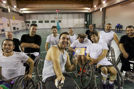 group of smiling disabled basketball players on a wheelchair take a selfie in a basketball courtの写真素材