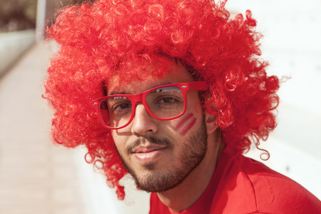 portrait of fan with red wig and glasses sitting on the stands of a stadiumの写真素材