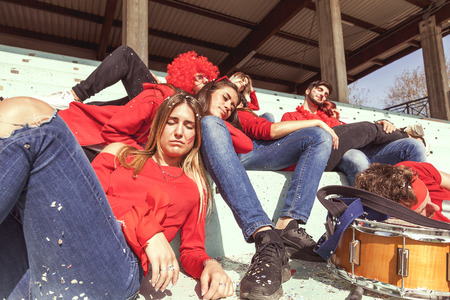 Young group of supporter fans dressed in red color relaxing lying down in the stands after the matchの写真素材