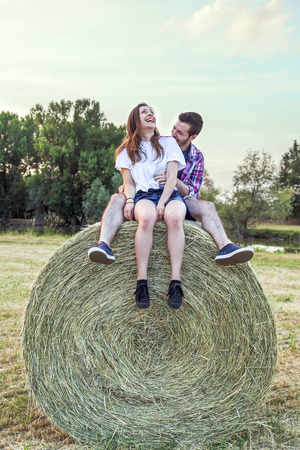Couple of lovers having fun outdoors on a summer sunset sitting on a sheaf of hayの写真素材