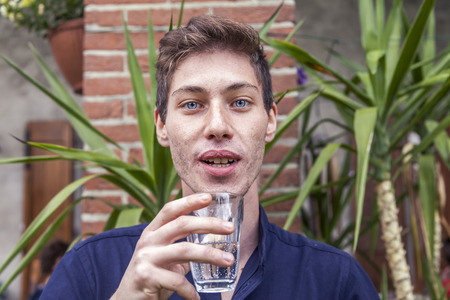 portrait of a young man while drinking a glass of fresh water at an outdoor partyの写真素材