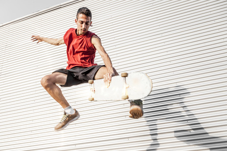 young skateboarder jumps up with his board in front of a metal background on the roofs of an abandoned buildingの写真素材
