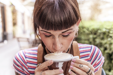 young woman with blue eyes gets her lips dirty with cream while drinking an italian cappuccinoの写真素材