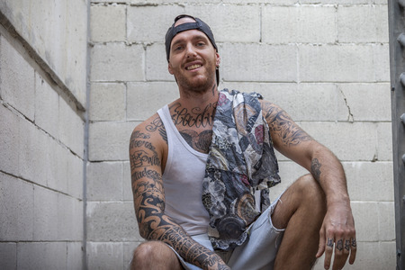 young caucasian tattooed singer rap posing sitting on the steps of a metal ladderの写真素材