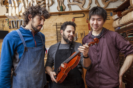 group of craftsmen violinmakers testing a new violin in their laboratory