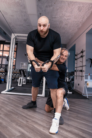 two friends athletes have fun while exercising at the cables in the gymの写真素材