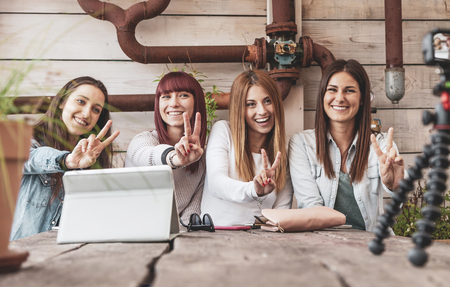 four young  vloggers talking on the camera leaning against a small tripod outdoorsの写真素材