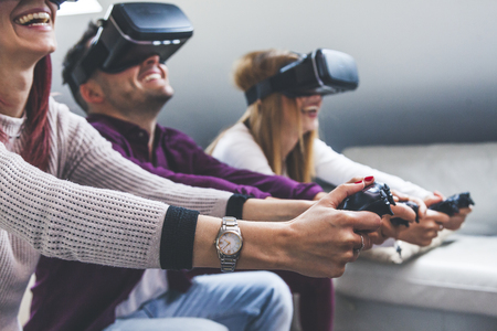 Young happy three friends playing video games virtual reality glasses in their apartment - concept of cheerful people having fun with new trends technologyの写真素材