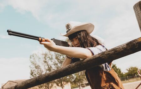 Portrait of a beautiful Chinese female cowgirl shooting with a weapon in the wild west behind a wooden fenceの写真素材