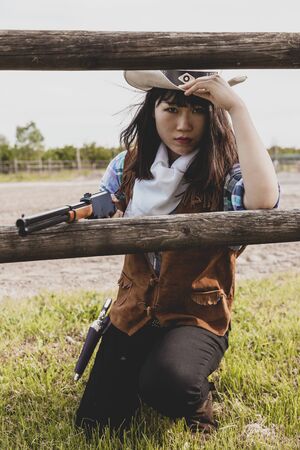 Portrait of a beautiful Chinese female cowgirl shooting with a weapon in the wild west behind a wooden fenceの写真素材