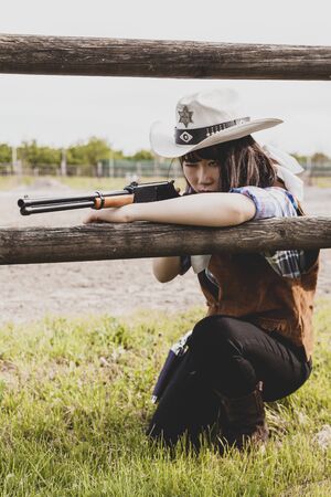 Portrait of a beautiful Chinese female cowgirl shooting with a weapon in the wild west behind a wooden fenceの写真素材