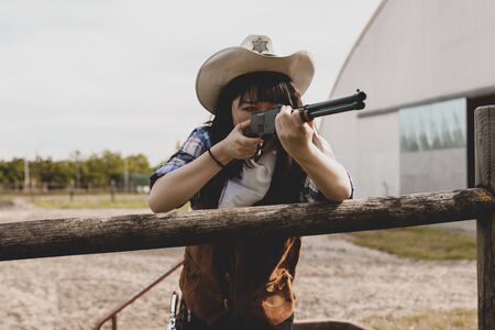 Portrait of a beautiful Chinese female cowgirl shooting with a weapon in the wild west behind a wooden fenceの写真素材