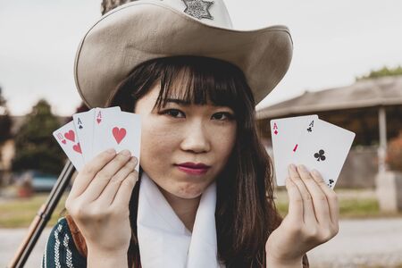 Portrait of a beautiful Chinese female cowgirl while playing with poker cards sitting outdoorsの写真素材