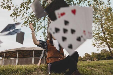 Portrait of a beautiful Chinese female cowgirl while playing with poker cards sitting outdoors