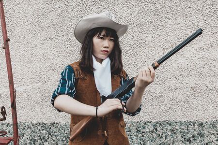 Portrait of a beautiful armed Chinese female cowgirl posing near an old carriage