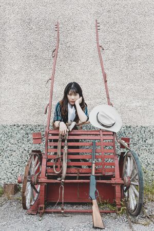 Portrait of a beautiful armed Chinese female cowgirl posing near an old carriageの写真素材