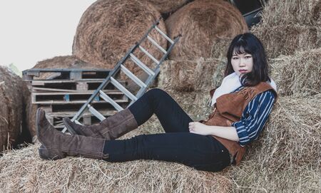 Portrait of a beautiful armed Chinese female cowgirl posing on sheaves of strawの写真素材