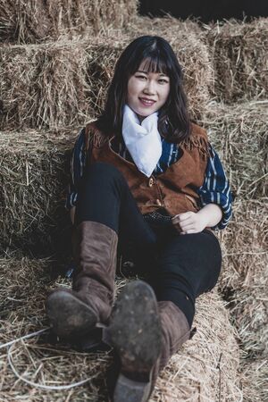 Portrait of a beautiful armed Chinese female cowgirl posing on sheaves of strawの写真素材