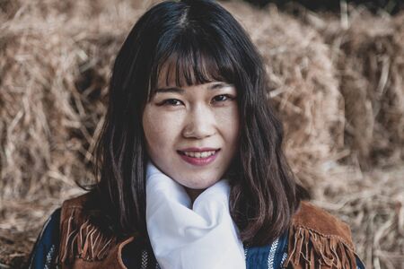 Portrait of a beautiful armed Chinese female cowgirl posing on sheaves of strawの写真素材