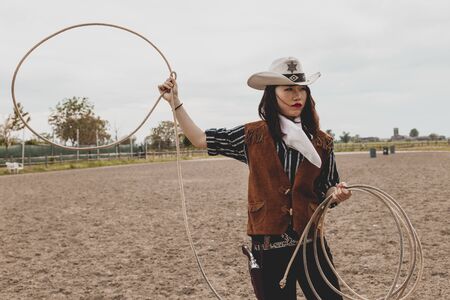 pretty Chinese cowgirl throwing the lasso in a horse paddock on a wild west farm