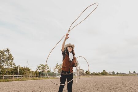 pretty Chinese cowgirl throwing the lasso in a horse paddock on a wild west farm