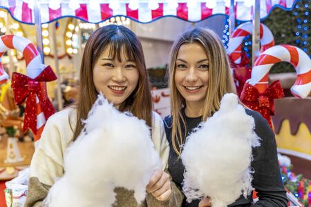 couple of young multi-ethnic women eating cheerful cotton candy at a party. concept of millennial generation and healthy enjoymentの写真素材