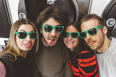 group of young friends wearing green sunglasses having fun taking a selfie in a public laundryの写真素材