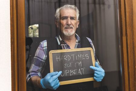 single mature man quarantined by coronavirus at window shows a message of hope on a blackboard