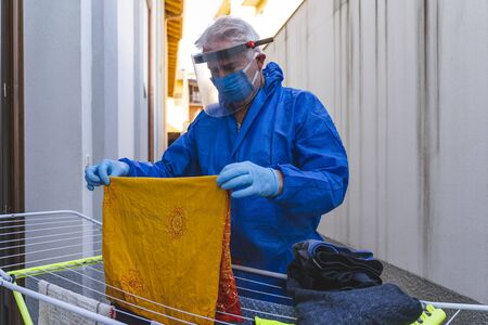 single man in quarantine dressed in protective suit is doing laundry during the coronavirus emergencyの写真素材