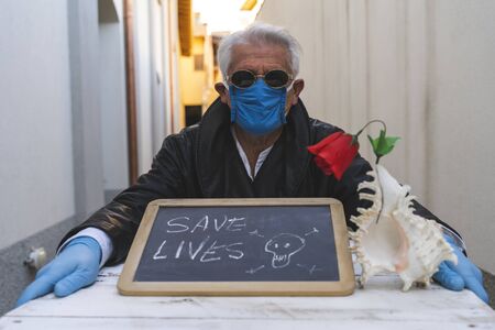 adult man with mask sitting at a table is showing a positive message written on a blackboard during...