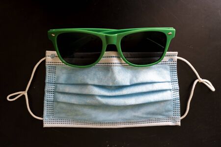 Face mask or surgical mask lays on a blackboard with green sunglasses like a face. Coronavirus...