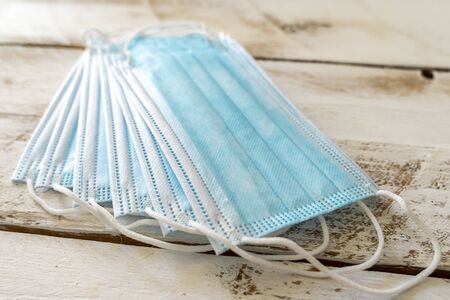 a lot of face mask or surgical mask lays on a wooden white table. Coronavirus COVID-19 diseases...