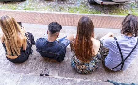 group of multiracial friends sitting on a marble staircase using smartphones to share content on...