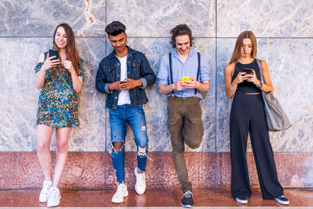 group of multiracial friends in front of a wall using smartphones to share content on social networksの写真素材