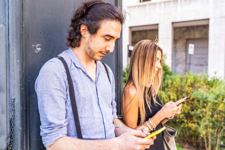 couple of multiracial friends in front of a newsstand using smartphones to share content on social networksの写真素材