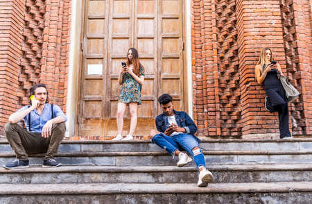 group of multiracial friends sitting on a marble staircase using smartphones to share content on...