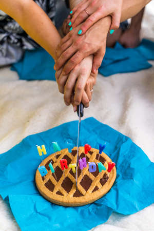 multiethnic group of hands are cutting a birthday cake outdoors sitting on the grassの写真素材
