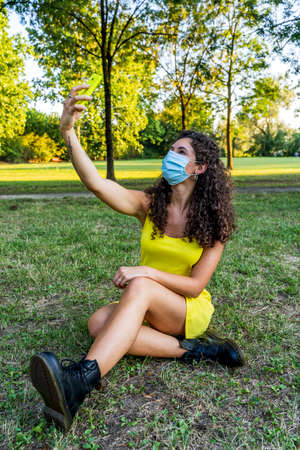 pretty young woman taking a selfie wearing an anti contagion face mask during the covid-19 emergencyの写真素材