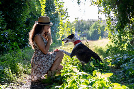 young woman with her dog is walking on a path surrounded by greenery in the countryside