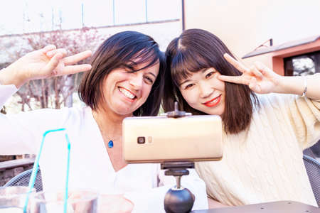 Young female friends multi-ethnic taking a selfie with smartphone during an outdoor aperitifの写真素材