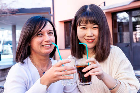 Young female friends multi-ethnic take an aperitif outdoors while talking and laughingの写真素材
