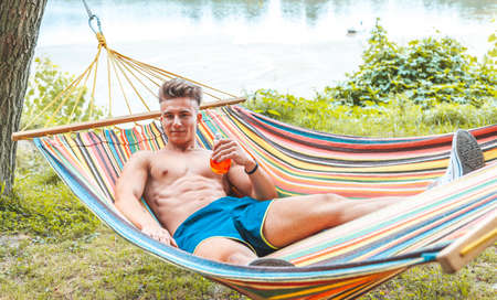 young muscular adult drinking a red drink lying in a hammock. youth summer vacation conceptの写真素材