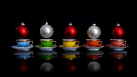 christmas balls over colorful cups on black background. Christmas spirit concept