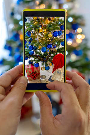 a woman photographs decoration on Christmas tree with his smartphone. concept of the Christmas atmosphereの写真素材
