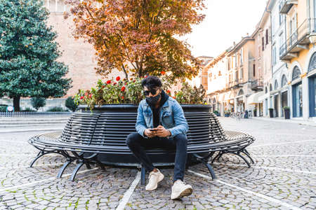 young adult with protective masks using smartphones to share content on social networks outdoorsの写真素材